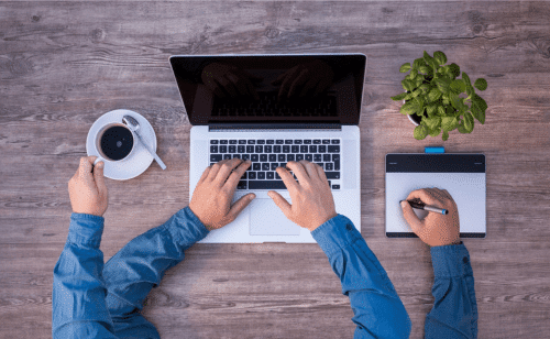 Frau mit vier Armen, die am Laptop sitzt, Kaffee trinkt und Dinge aufschreibt und offensichtlich gerade organisiert.